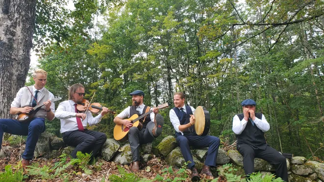 Five men sitting on a rock wall, playing string instruments